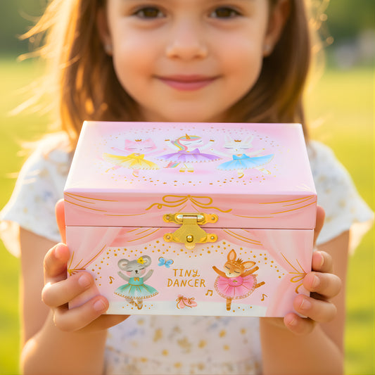 Child holding a pink jewelry box with ballerina designs outdoors.