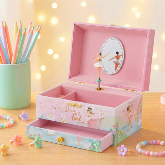 Pink music box with ballerina design on a wooden surface with colorful pencils and flowers.
