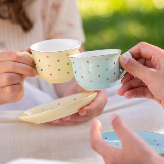 Two little girls toasting with hand-painted pastel porcelain teacups with gold polka dots at an outdoor tea party