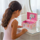 Young girl playing with a pink music box featuring fairy designs.