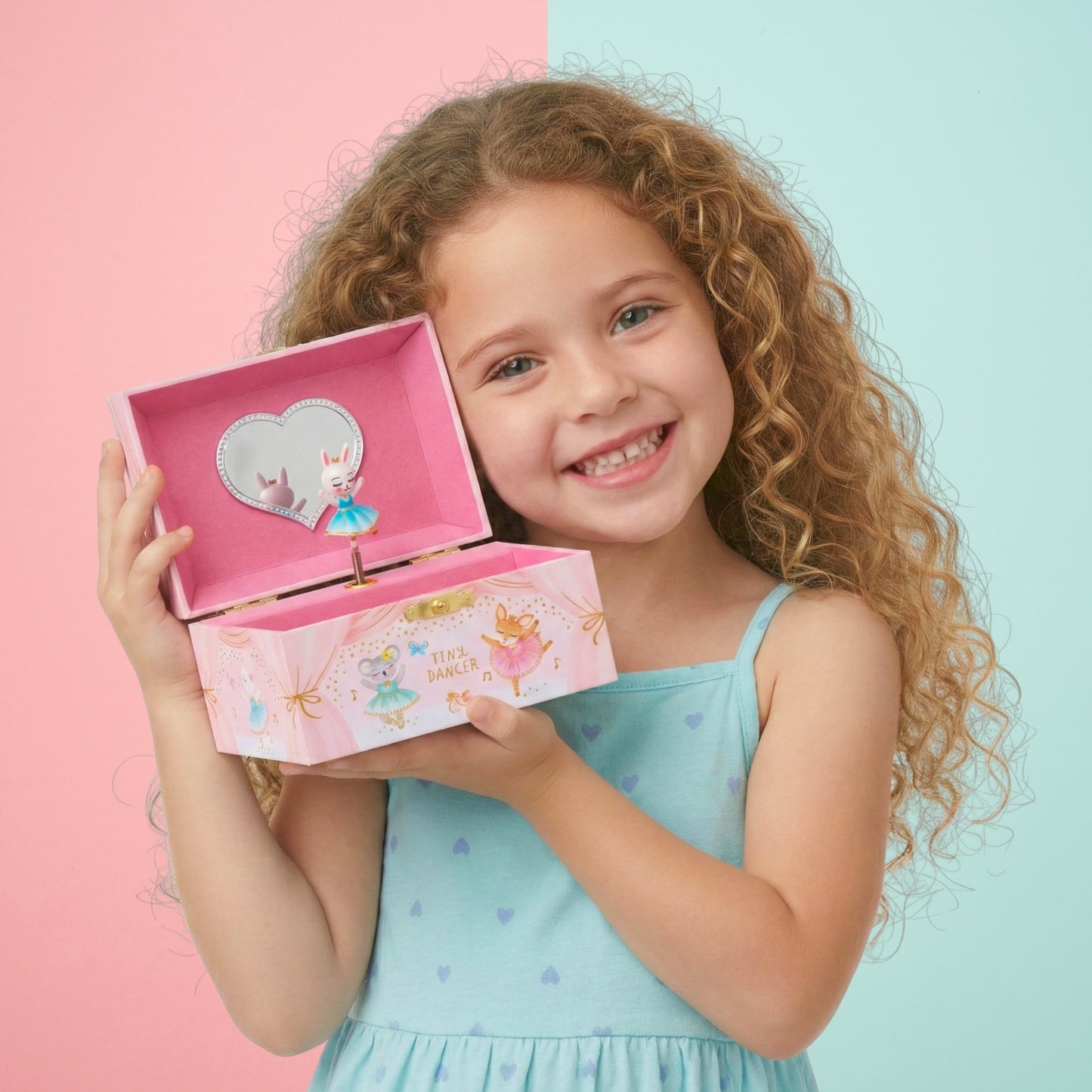 Young girl holding a pink jewelry box with a heart-shaped mirror on a two-tone pink and blue background