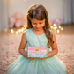 Young girl in a light blue dress holding a pink jewelry box with ballerina design.