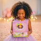 Young girl in a purple dress holding a pink and yellow gift box with a princess design.