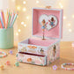 Pink fairy-themed music box with a drawer on a wooden surface with colorful pencils and flowers.