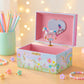 Unicorn-themed music box with pastel colors on a wooden surface with decorative lights in the background.