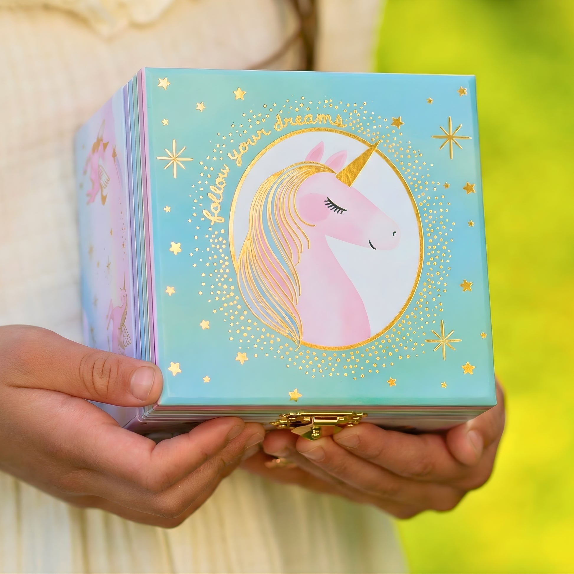 Person holding a unicorn-themed jewelry box with 'Follow Your Dreams' text.