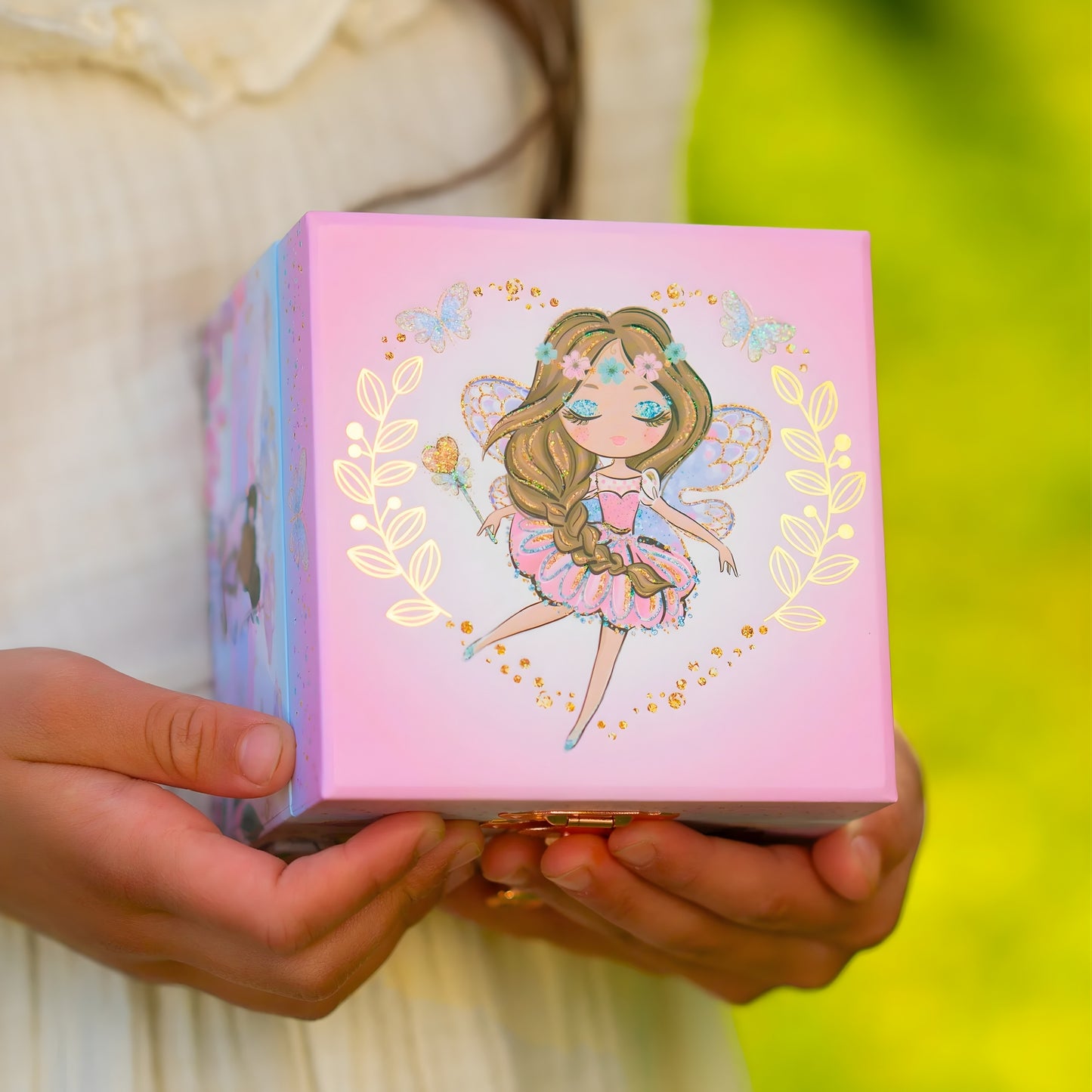 Person holding a pink box with a fairy illustration on a blurred green background