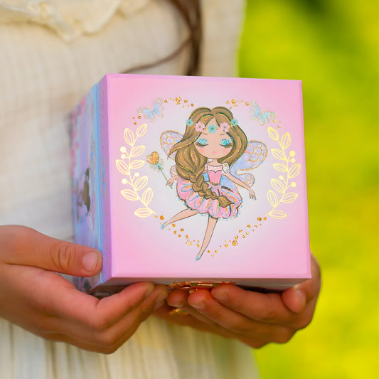 Person holding a pink box with a fairy illustration on a blurred green background