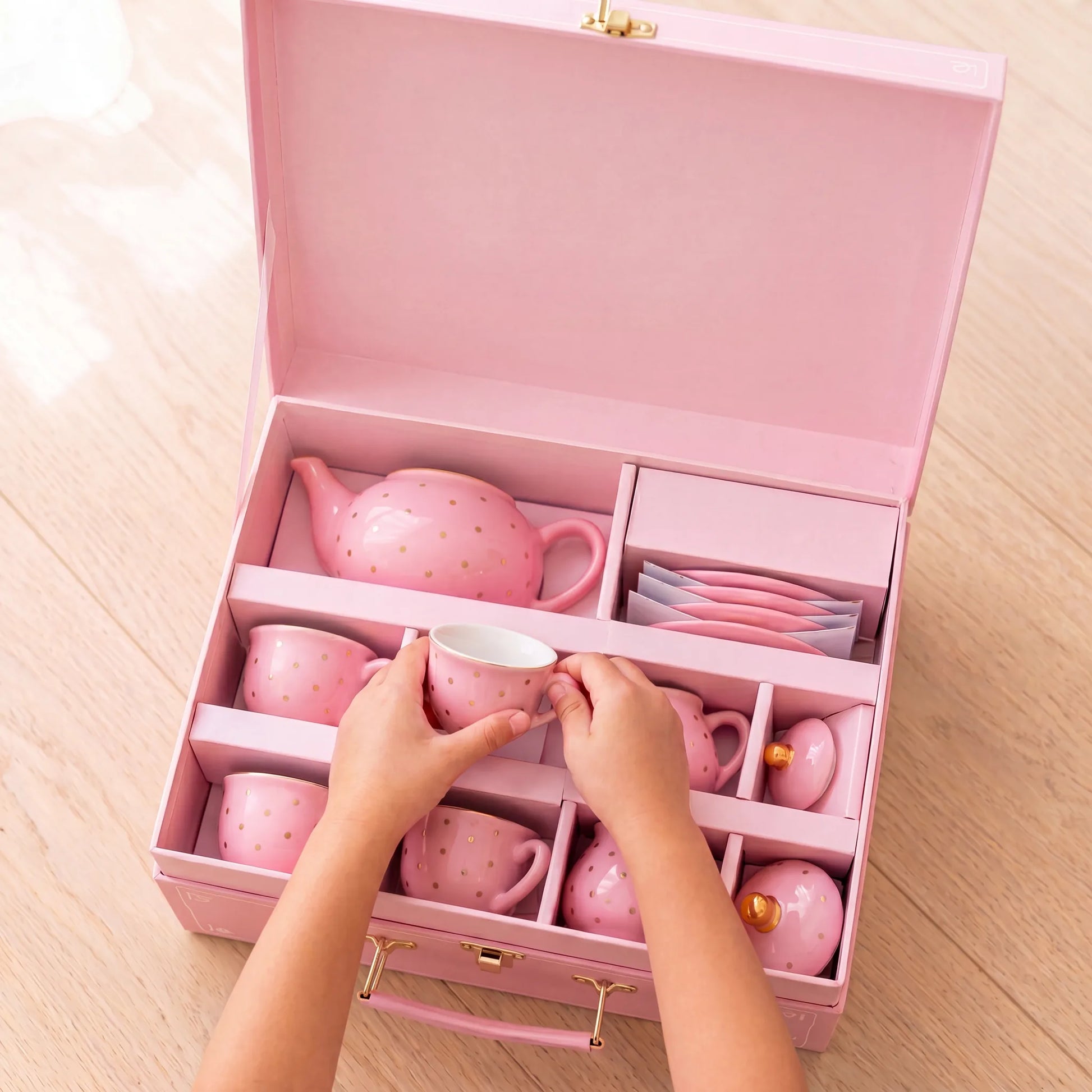 Child packing the pink porcelain tea set into its pink storage suitcase with handle