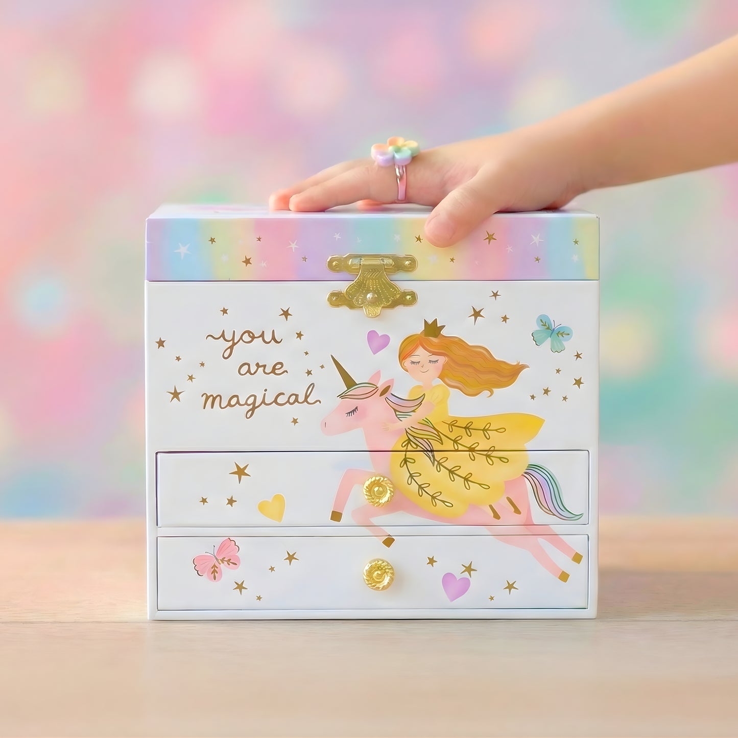 Jewelry box with a fairy and unicorn design, held by a hand against a colorful background.