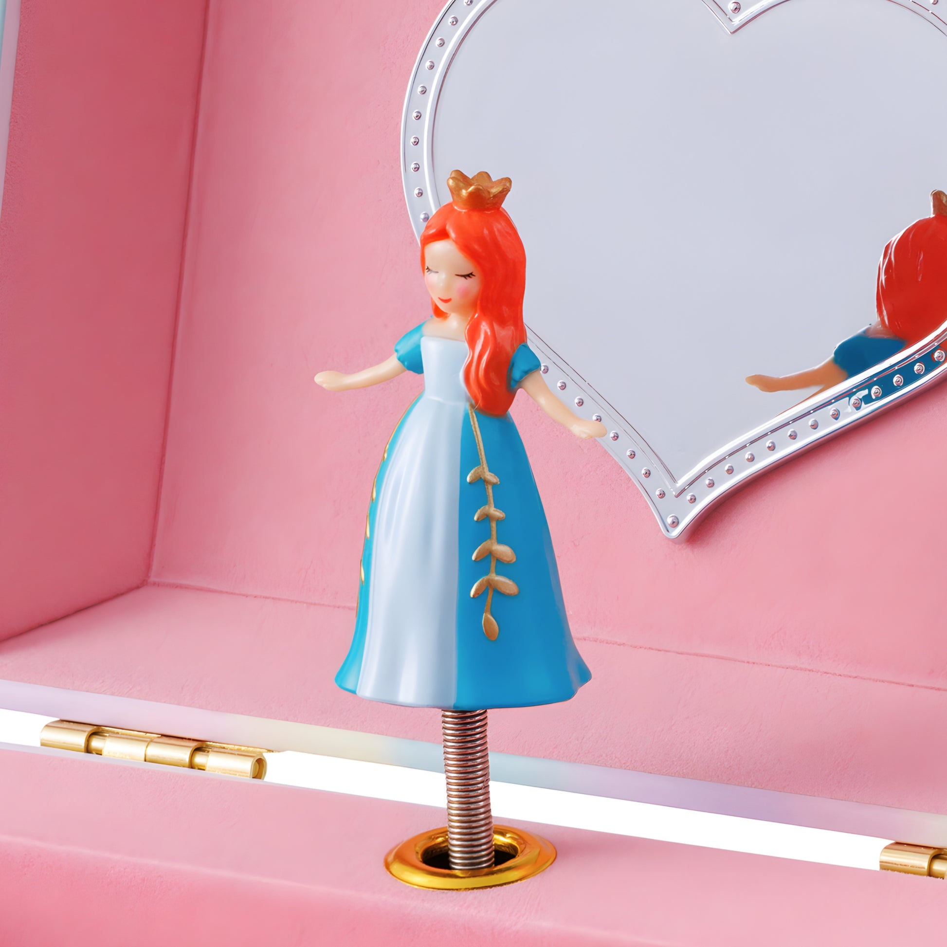 Toy figure of a princess with red hair and blue dress on a pink cushion